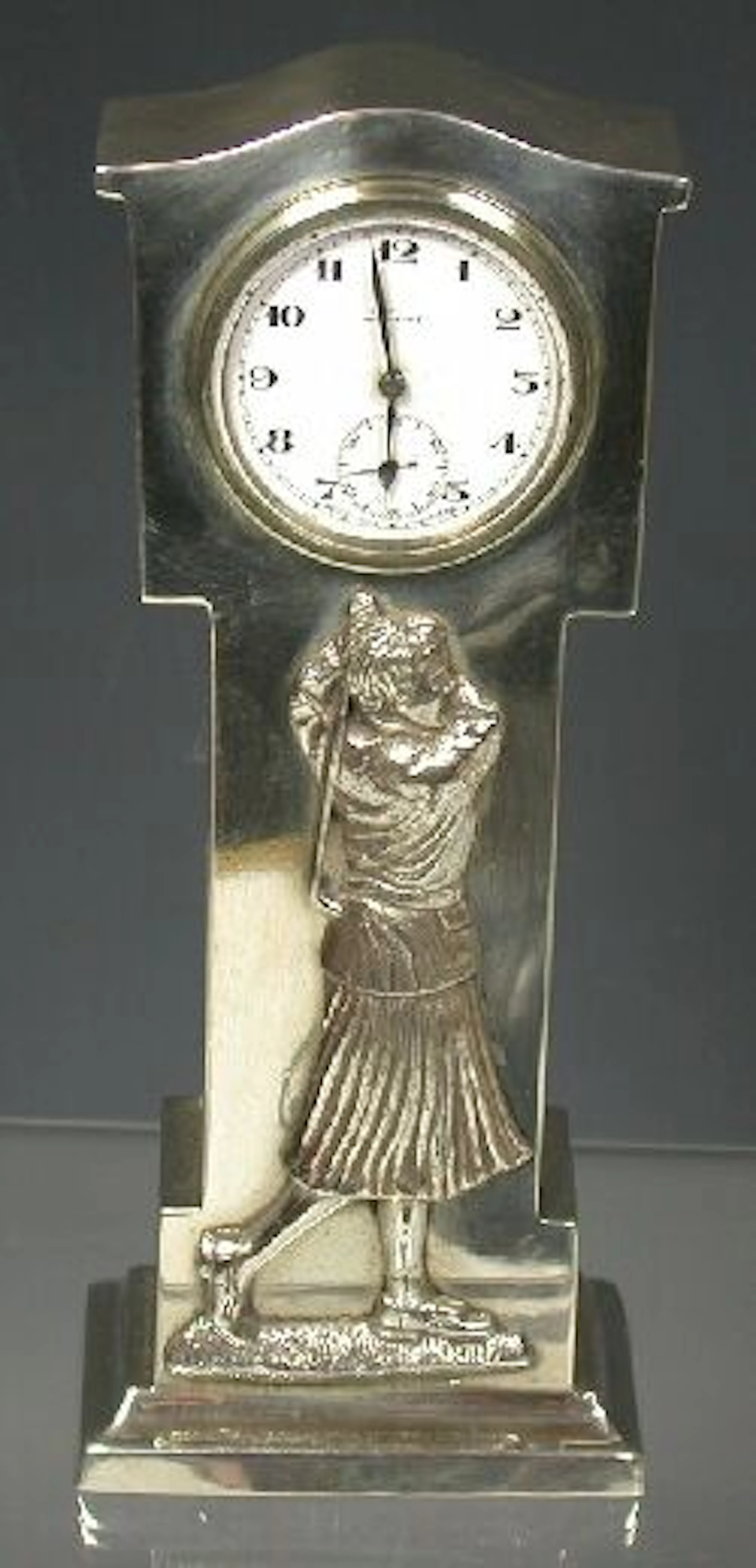 A golfing subject clock,, the silver case, formed as a miniature longcase clock, relief-decorated to the frieze with a lady golfer...