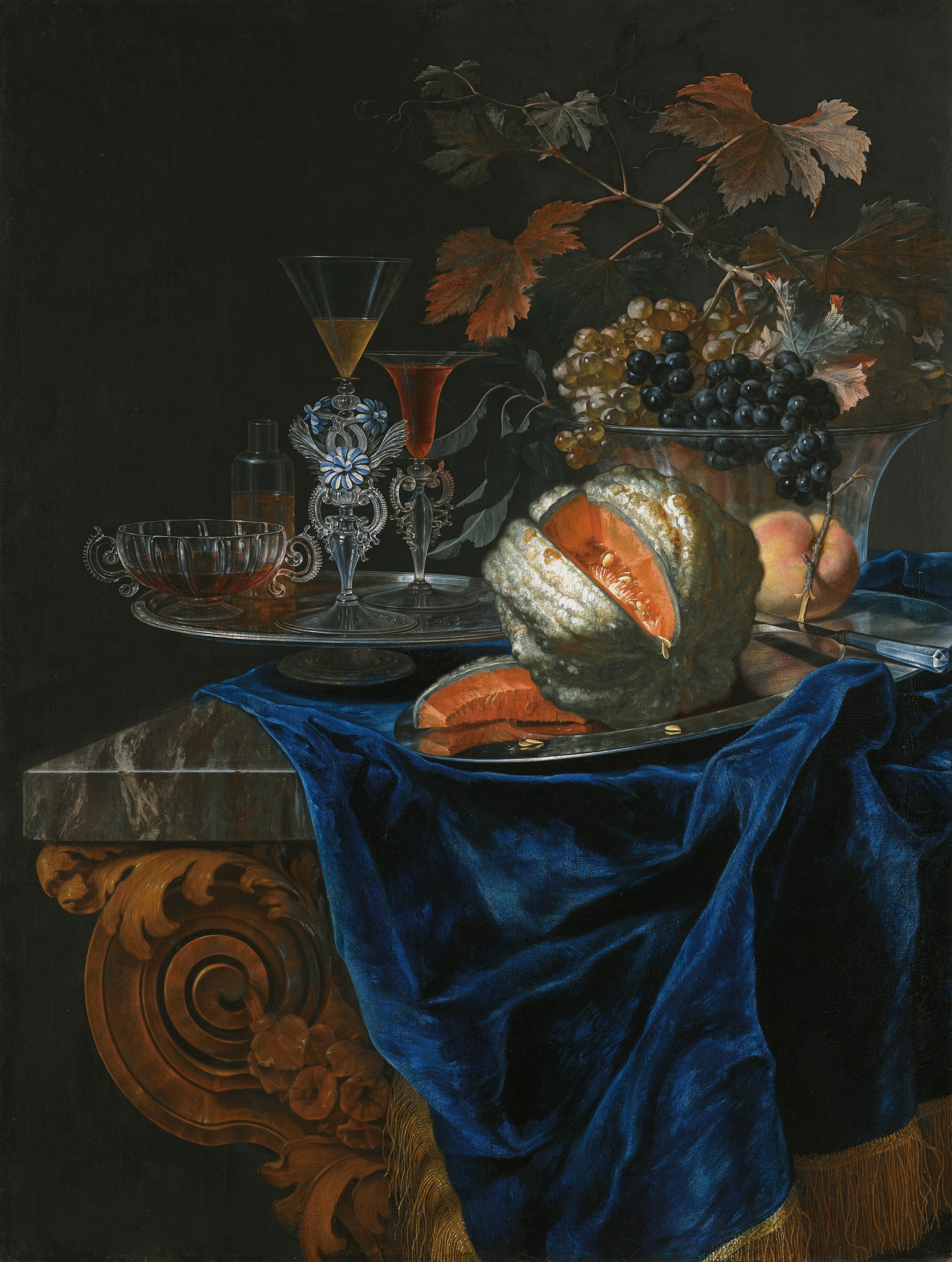 still life with a melon and a peach on a silver platter, together with a glass bowl of grapes and a tray of assorted glassware on a marble table top partly draped with a blue cloth
