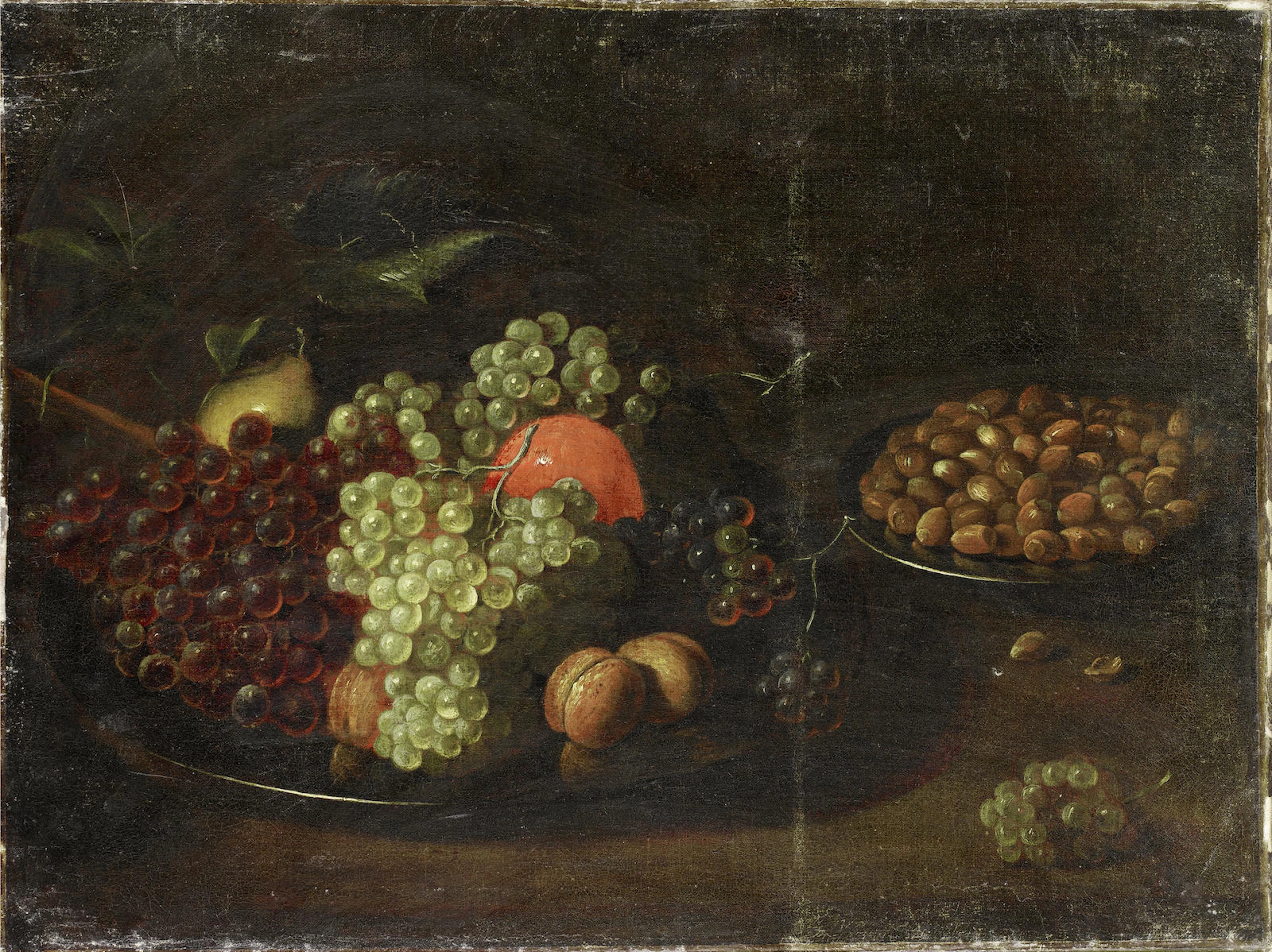 A pear, an orange, grapes and hazelnuts on pewter plates on a table top
