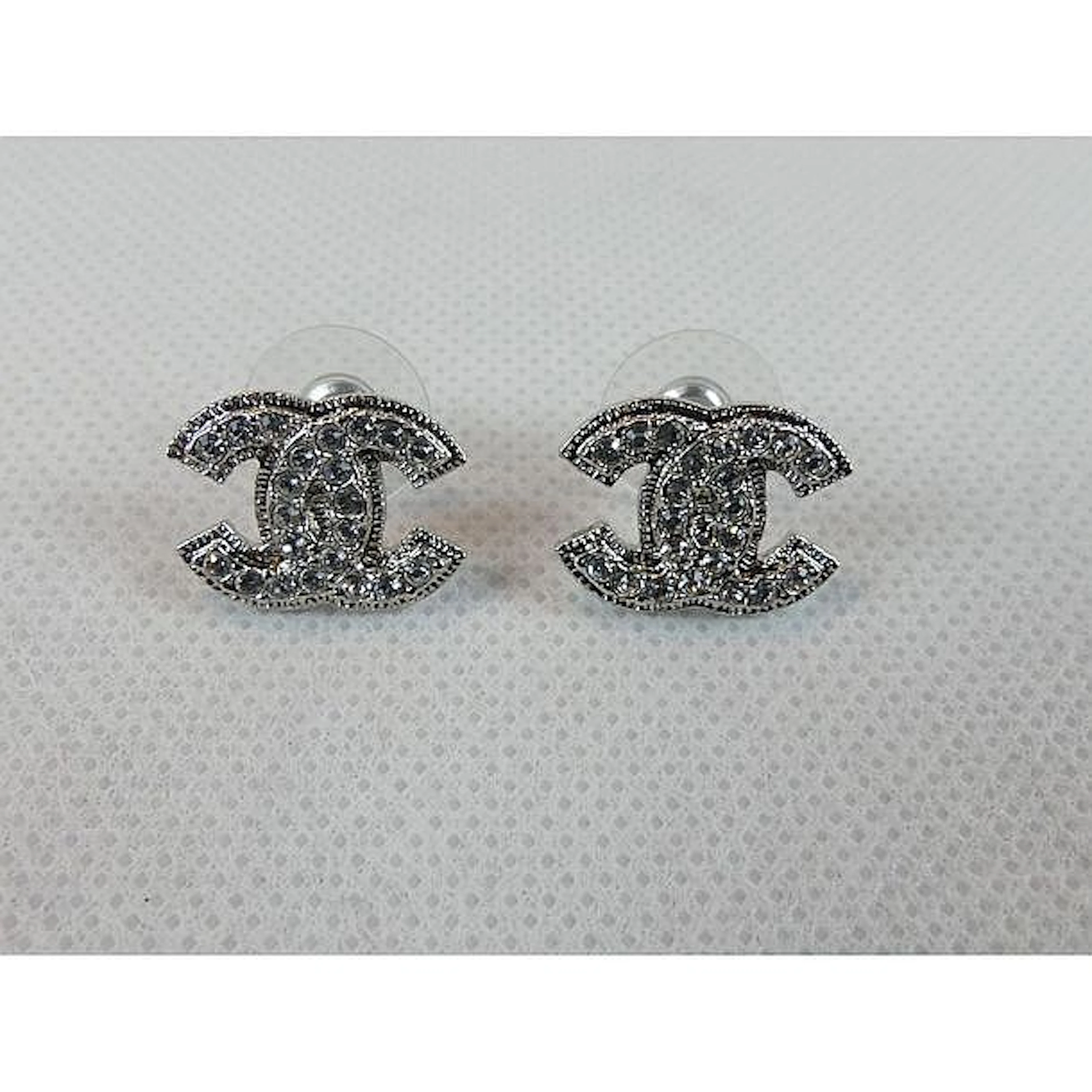 CHANEL. Paire de boucles d?oreilles en métal argenté ornées du sigle serti