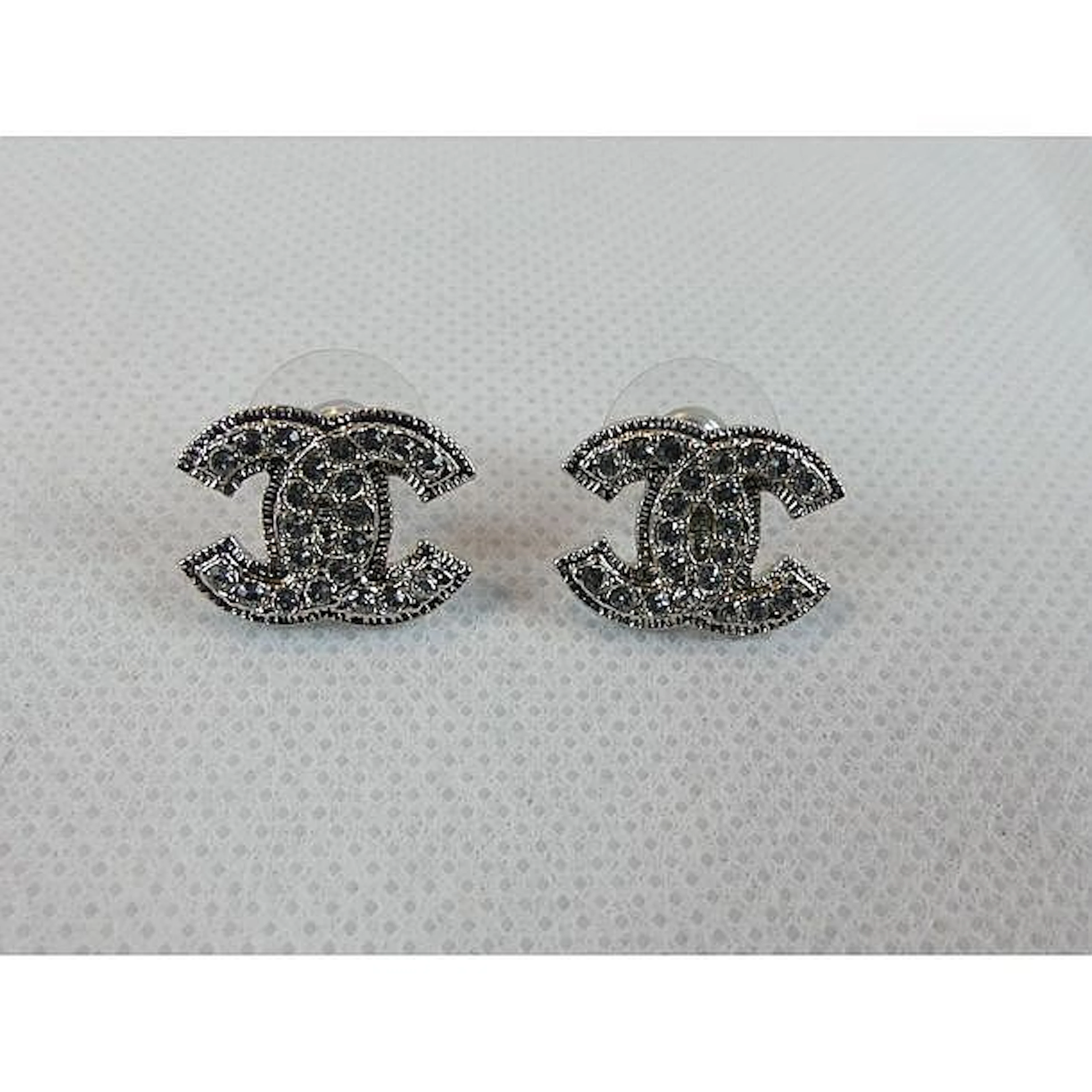 CHANEL. Paire de boucles d?oreilles en métal argenté ornées du sigle serti