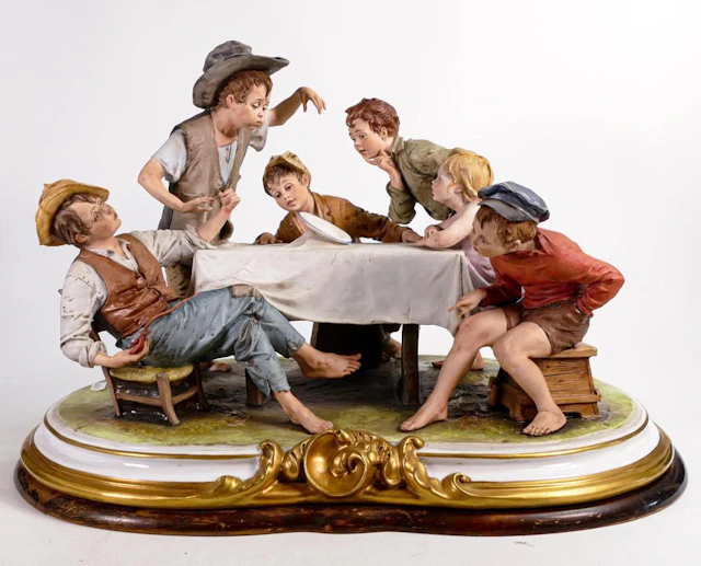 A large Capodimonte group of 6 children sitting around a table watching a m