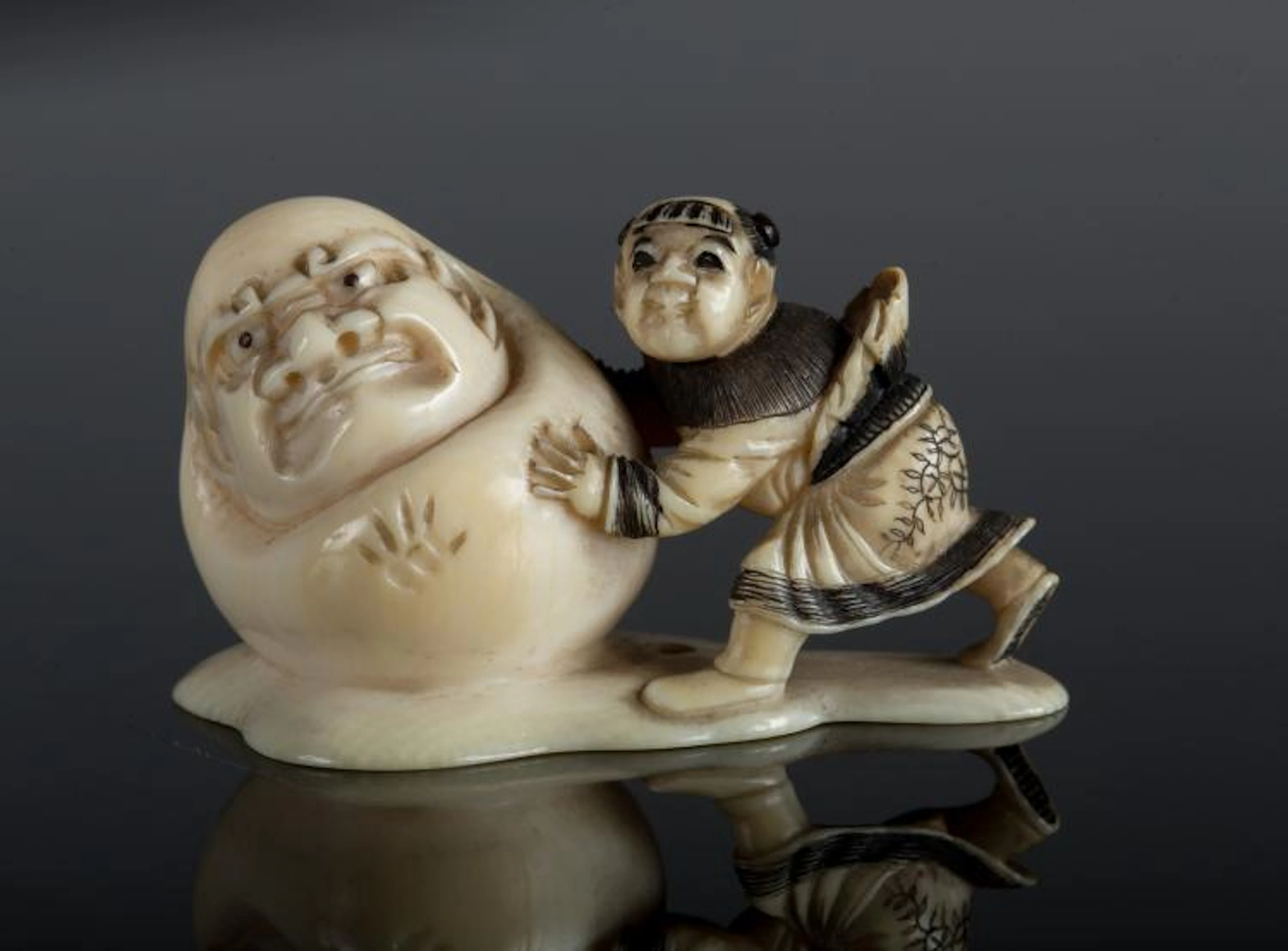 Arte Giapponese An ivory netsuke depicting a child pushing a Daruma doll