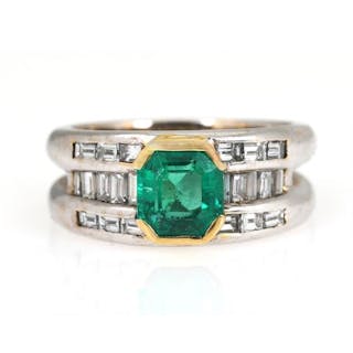 An emerald and diamond ring set with an emerald flanked by numerous