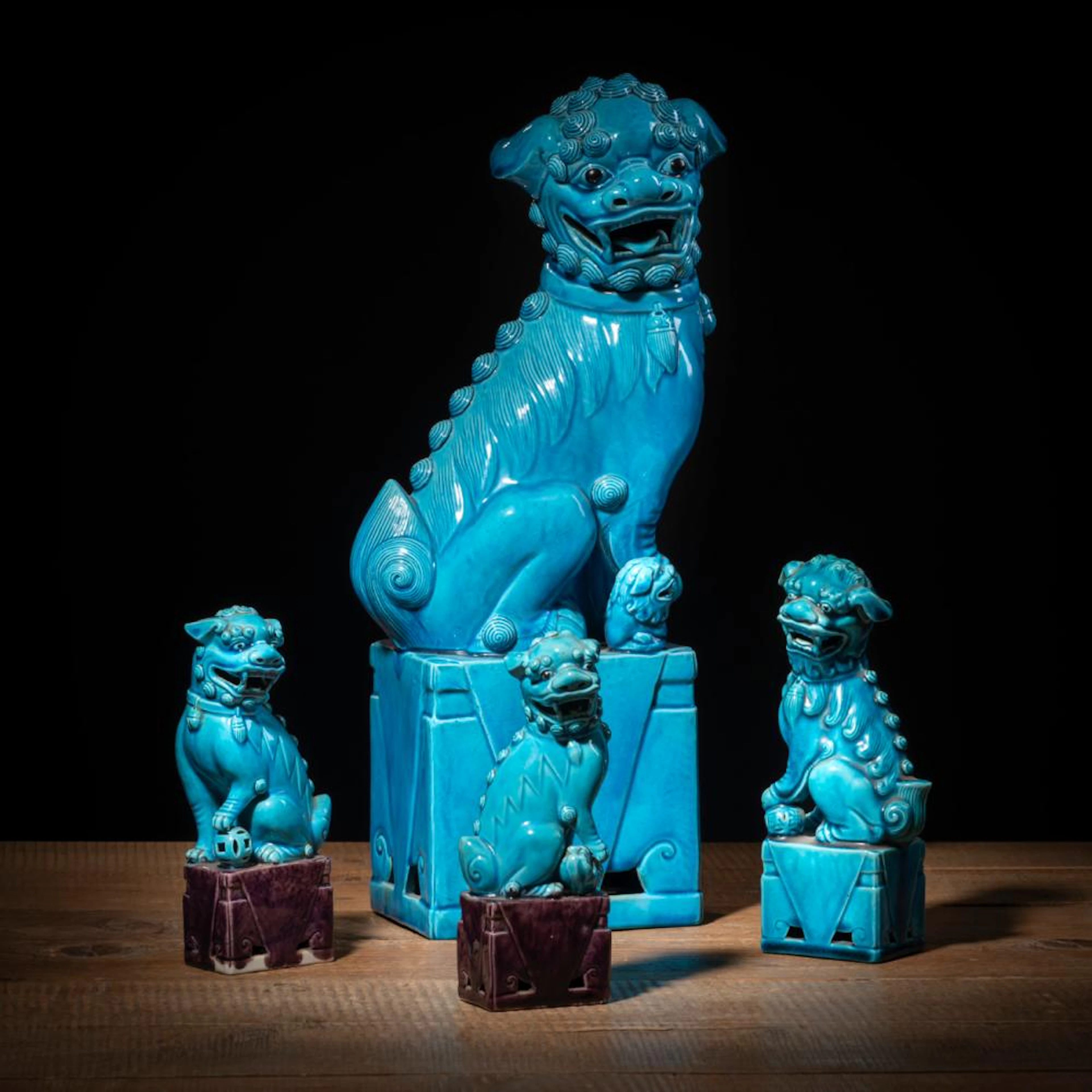 FOUR TURQUOISE PARTLY AUBERGINE GLAZED PORCELAIN SEATED LIONS ON PEDESTAL