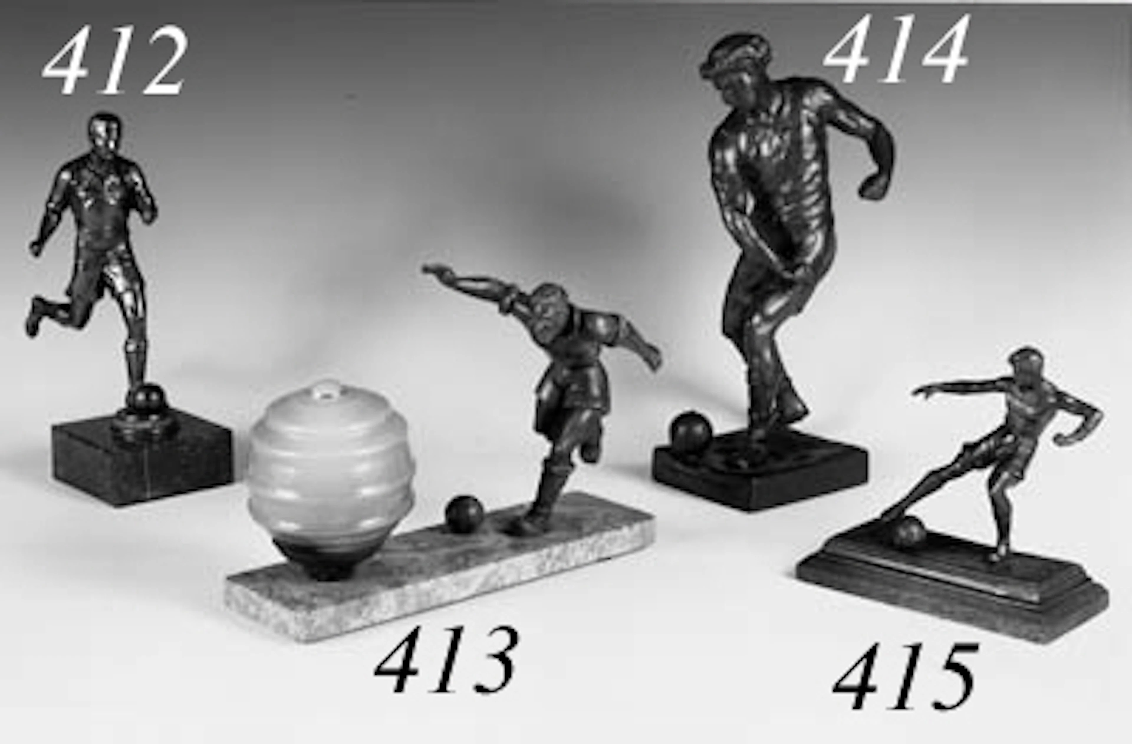 An Art Deco style table lamp formed as a green-painted spelter figure of a footballer about to kick a football with his right foot, with mottled yellow glass