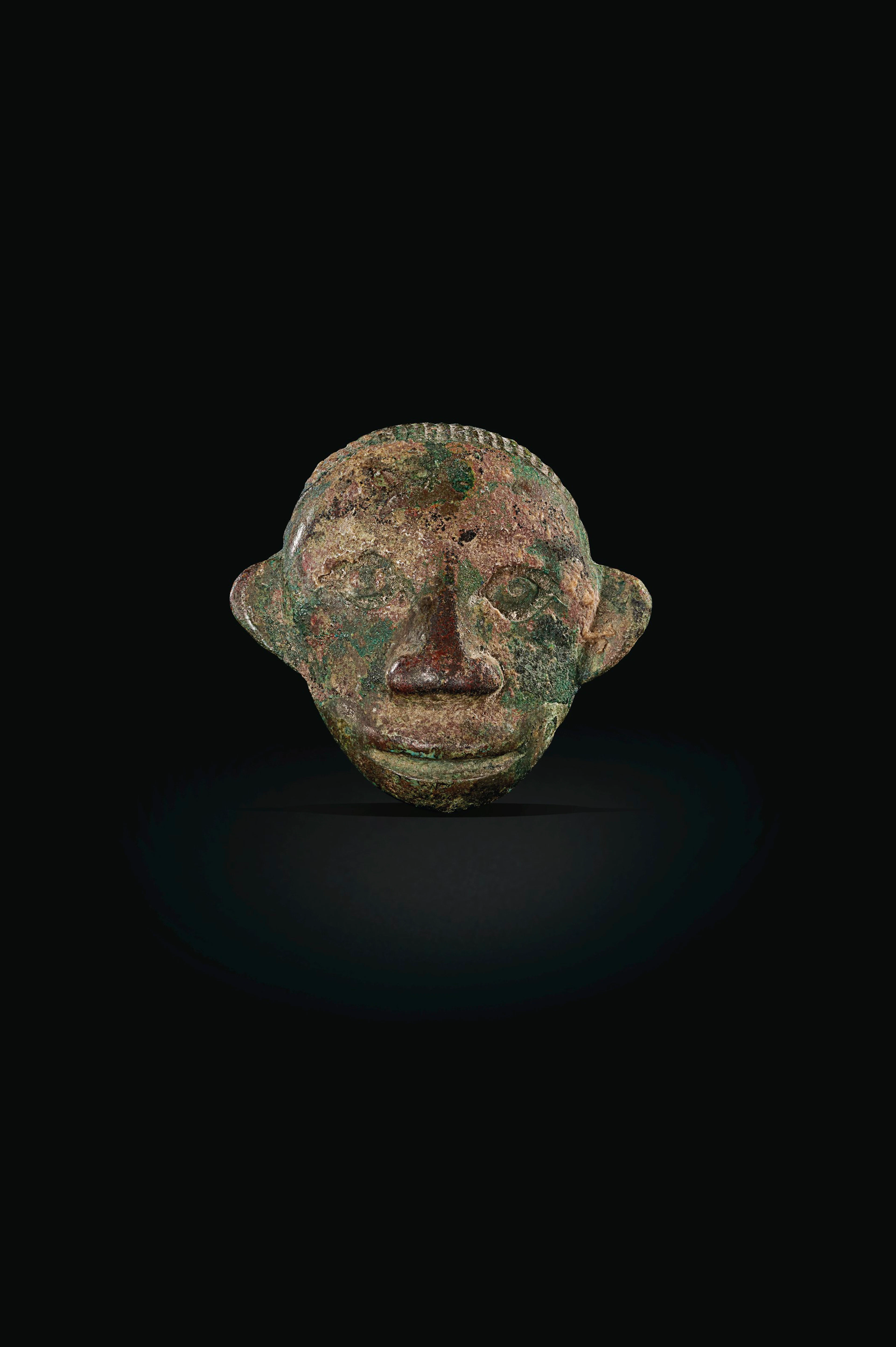 AN UNUSUAL SMALL BRONZE HUMAN MASK-FORM HARNESS ORNAMENT