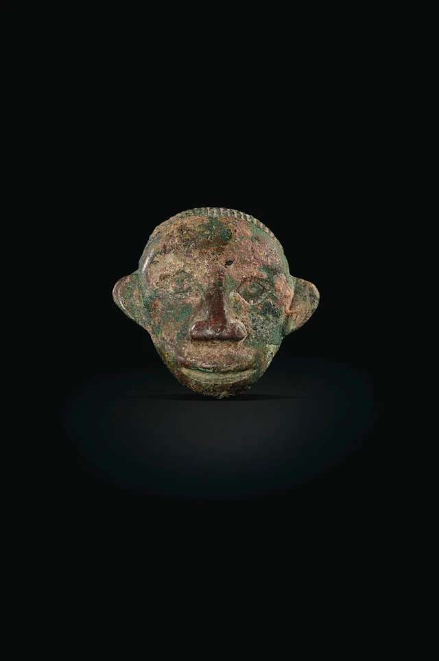 AN UNUSUAL SMALL BRONZE HUMAN MASK-FORM HARNESS ORNAMENT