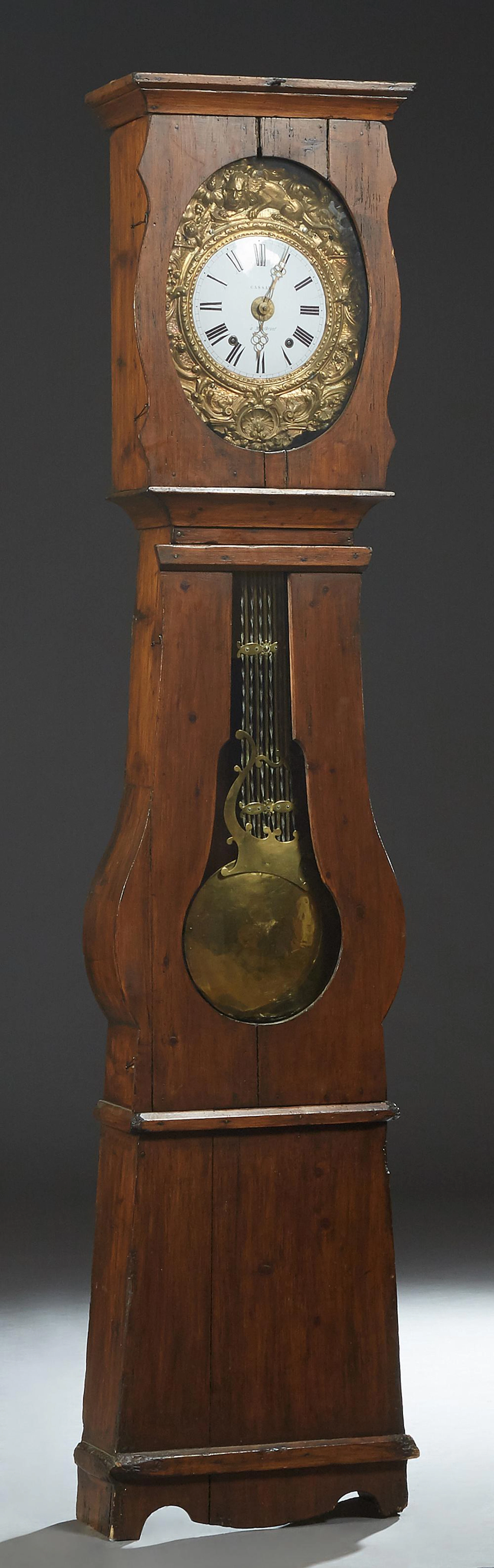 French Provincial Carved Pine Tallcase Clock, 19th c., the stepped crown over a brass repousse face with scroll and floral decoratio...