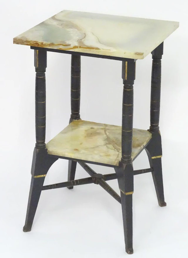An Aesthetic movement table with two onyx tiers and an ebonised frame with gilt highlights, the spla