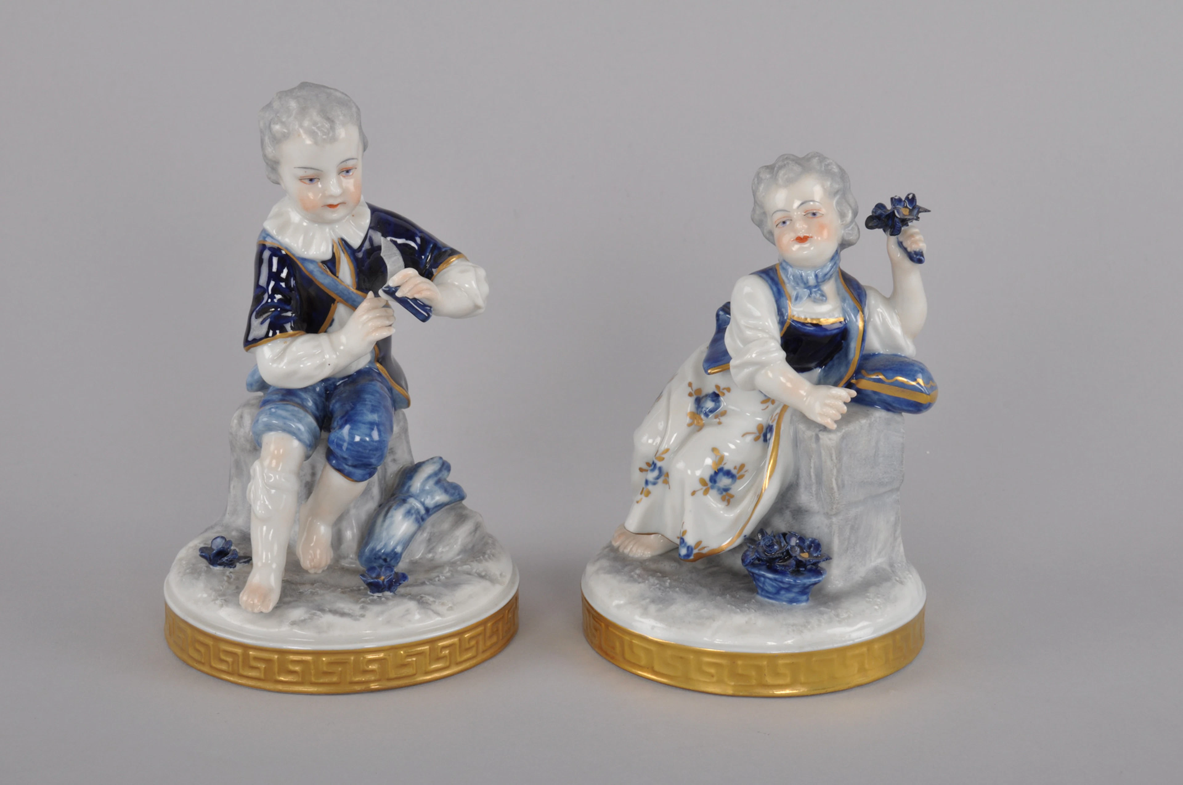 ÄLTESTE VOLKSTEDTER PORZELLANMANUFAKTUR. 2 Porzellanfiguren " Mädchen sitzend mit Blumenstrauß" un " Knabe sitzend mit Sichel". Nach 1945.