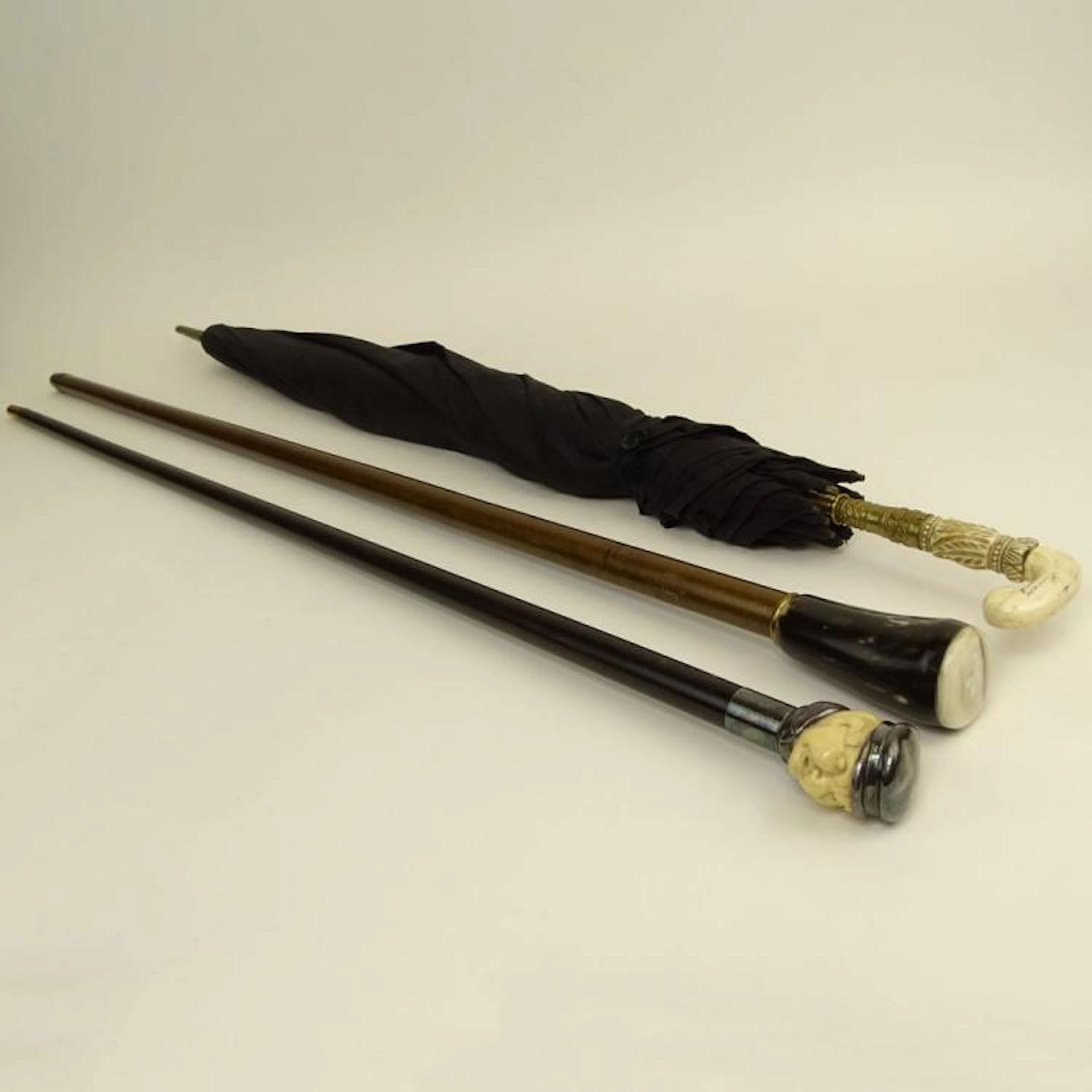 Lot of Three (3) Antique Umbrella and Canes. The umbrella and one stick with Carved Ivory Handles, the other stick with horn handle. Wear, cracks, antique condition. Tallest measures 37" H