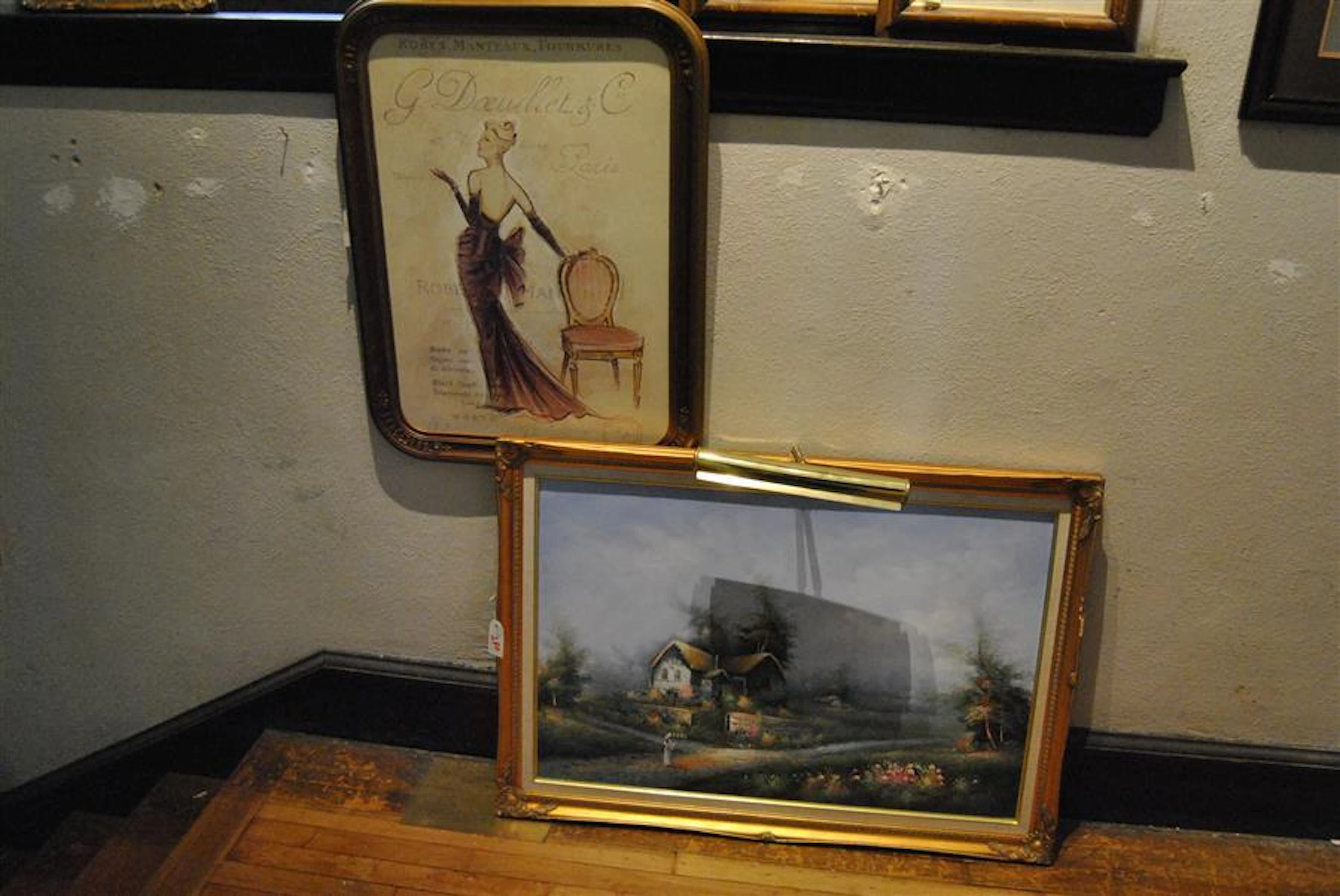 Two pieces of wall art: decorative fashion print and a landscape scene with a cottage in a gilt frame