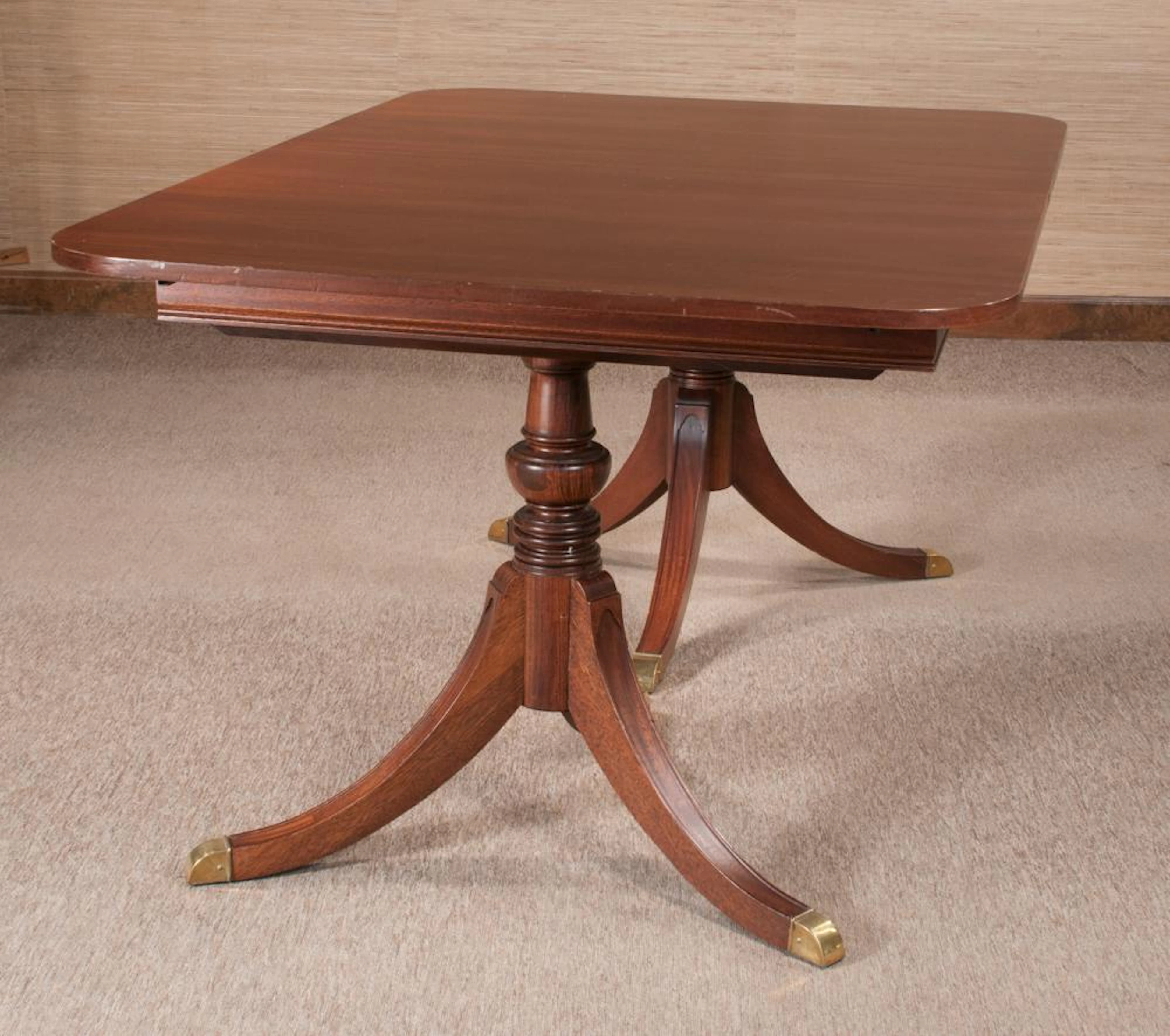 Sheraton style mahogany dining table with two hidden leaves, bases have an urn shaped column with three splay legs with brass caps, by The White Furniture Co, 62" wide, 42" deep, 30" high